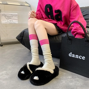 Close-up of black fuzzy slippers with white pom poms paired with white and pink socks