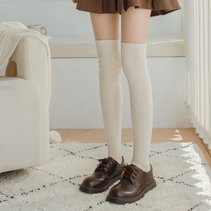 Detailed knit texture of white thigh-high wool leg warmers with cozy cable stitch pattern