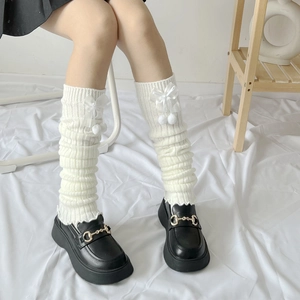 Nahaufnahme weißer Strick-Beinstulpen mit Satin-Schleifen und flauschigen Pompon-Details
