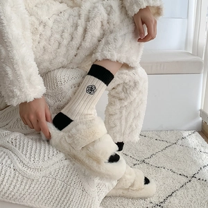 Detail of camellia flower embroidery on white wool socks and plush slippers in home setting