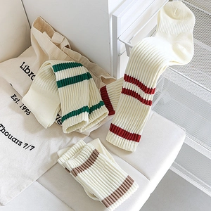 Detail of ribbed knit knee high socks with red and green stripes on cream fabric