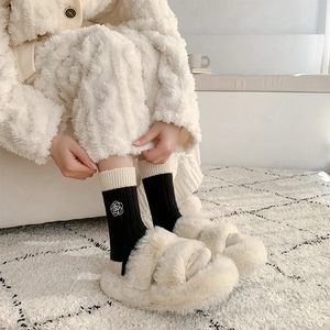 Detail of black wool socks with white rose embroidery and plush slippers in home setting