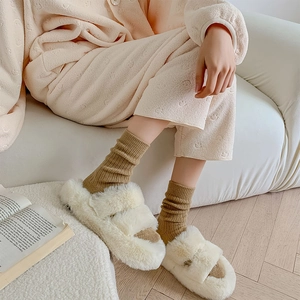 Dettaglio di pantofole in peluche bianco con calze marroni calde in un ambiente accogliente