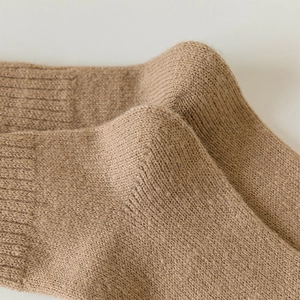 Close-up of beige wool over-knee socks showing thick ribbed knit texture and elastic cuffs