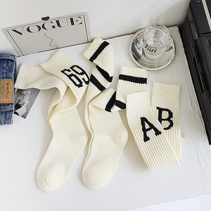 Détail de la texture des chaussettes hautes crème avec rayures noires et lettres