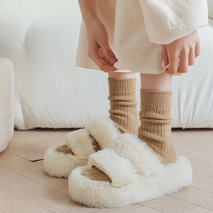 Dettaglio di pantofole platform in peluche con doppie fasce color crema e calzini marroni