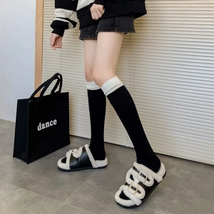 White knee-high slouch socks with layered cuffs paired with plush black sandals