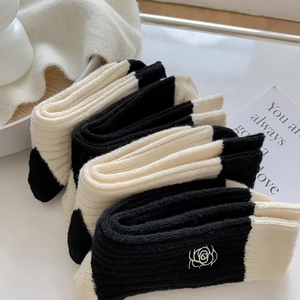 Close-up of white rose embroidery on black and white ribbed wool blend socks
