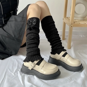 Details von schwarzen JK-Strickstulpen mit Satinschleifen und Plateau-Lederschuhen