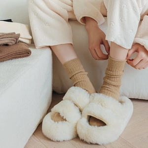 Dettaglio di pantofole in peluche crema e calze di lana color cammello calde