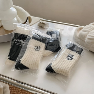 Detailed view of three pairs of bicolor rib-knit wool socks with camellia embroidery