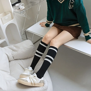 Close-up of black ribbed knee-high socks featuring white double stripes in varsity style