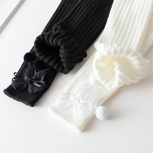 Detail von Strick-Stulpen mit Chiffonschleifen und Pompons in Schwarz und Weiß