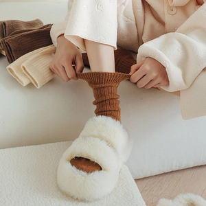 Dettaglio calzini in lana color caramello con pantofole di peluche in ambiente invernale
