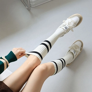 Detail of white ribbed knit knee high socks with black double stripes and casual sneakers
