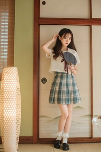 Detailed shot of white sailor top with red bow and plaid pleated skirt on a tatami mat