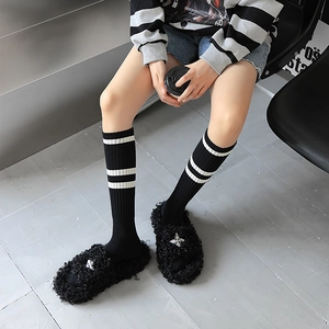 Détail de chaussons en peluche noire avec croix argentée et chaussettes rayées