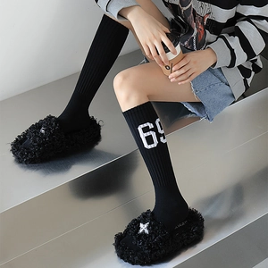 Détail de chaussons en peluche noire avec boucle croisée et chaussettes à rayures