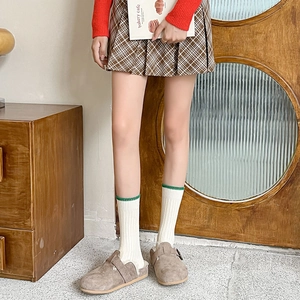Detail of brown suede mule shoes and white knit socks with green scalloped edges