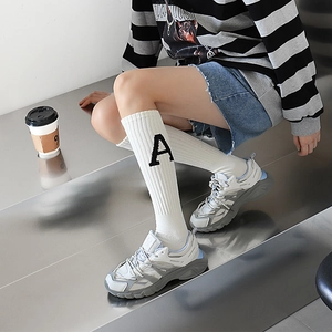 Gros plan de chaussettes hautes blanches avec lettre A noire et baskets chunky