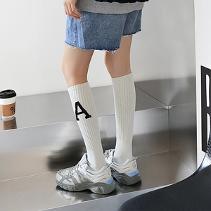 Détail de chaussette blanche en coton côtelé avec broderie lettre A et baskets grises tendance