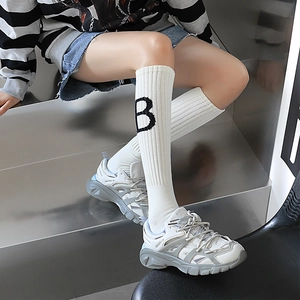 Détail de chaussettes montantes blanches avec jacquard lettre B et baskets à plateforme