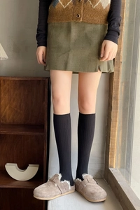 Detail view of black ribbed knee-high cotton socks with grey suede mule slippers