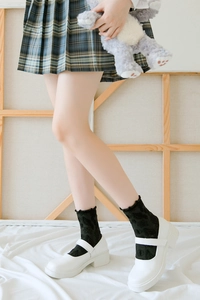 Gros plan de chaussettes noires en dentelle à bords volantés avec chaussures Mary Jane blanches