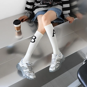 Détail de chaussettes mi-mollet côtelées blanches à lettres noires et baskets compensées