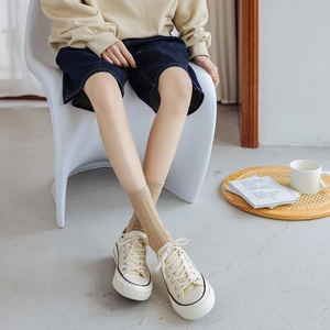 Detail of khaki cable knit mid-calf socks paired with classic white canvas shoes