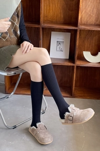 Detail of black knee-high ribbed cotton socks paired with casual brown suede shoes