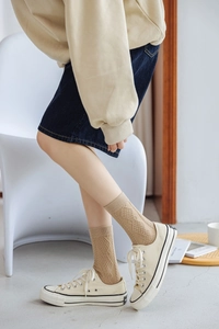 Detail of beige argyle knit cotton socks styled with sneakers and denim skirt