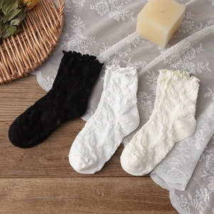 Détail des bords à volants et texture florale 3D sur chaussettes noires, blanches et crème