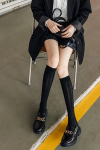 Close-up of black hollow knit knee-high socks paired with chunky gold chain loafers