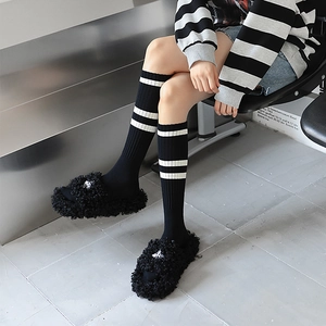 Chaussettes montantes rayées avec pantoufles en peluche noire dans un décor minimaliste
