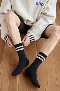 Détail de chaussettes noires mi-hautes avec rayures blanches sur un modèle assis