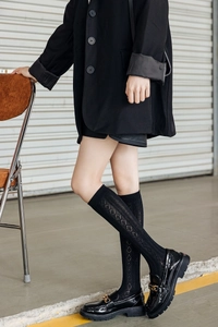Detail of black knee-high socks with diamond knit pattern and gold chain loafers