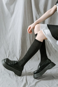 Détail de chaussettes hautes noires à motifs de cœurs et bords à volants avec mocassins