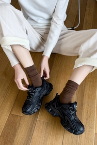 Detail of black platform sneakers with layered leather and mesh on wooden floor