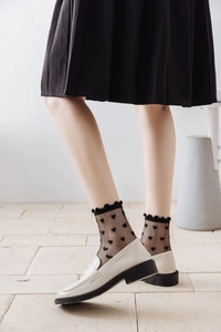 Detail of sheer black crew socks with heart pattern and ruffled cuffs styled with loafers