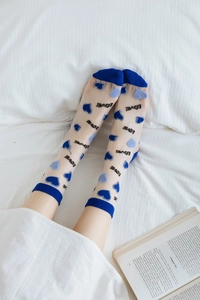 Detail of sheer mesh crew socks with blue heart patterns and LOVE text on soft bed