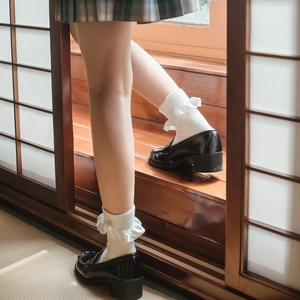 Japanese style white ruffle crew socks with black glossy leather loafers in a cozy room