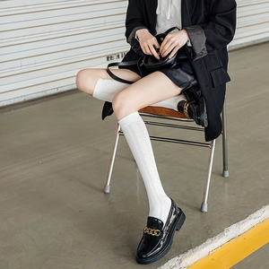 Detail of white diamond-patterned knee-high socks with black loafers and gold chain