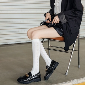 Detail of black platform loafers with gold chain and white hollow-out knee-high socks