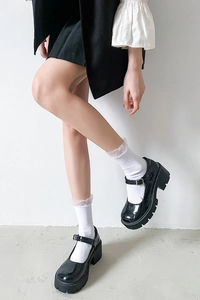 Close-up of black patent leather Mary Jane shoes with white lace ruffled crew socks