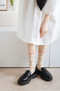 Detail of sheer white mid-calf socks with orange heart patterns and black loafers