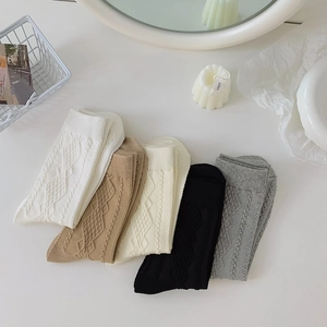 Detail of five pairs of cable knit crew socks in white, caramel, black, and grey tones