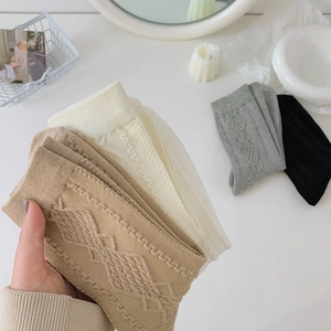 Detail of knit crew socks with argyle pattern in khaki, white, grey, and black colors