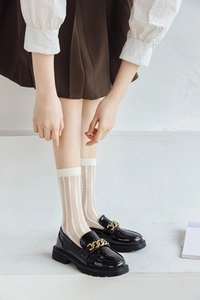 Detail of sheer white mesh crew socks with vertical stripes worn with black patent loafers