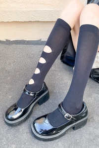 Détail de chaussettes noires ajourées portées avec des chaussures Mary Jane vernies